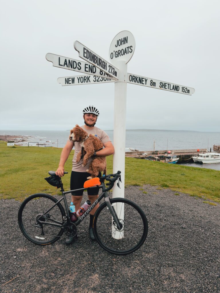 Tom with his bicycle and dog at the John O’Groats signpost